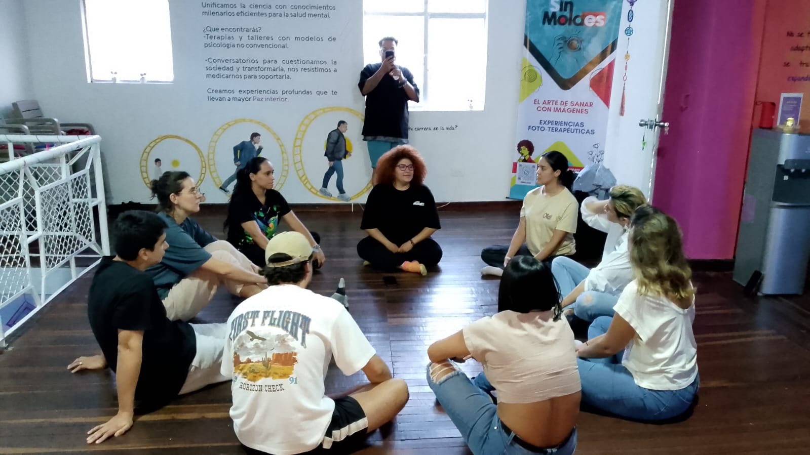 Participantes sentados en círculo en el piso de madera durante una sesión grupal